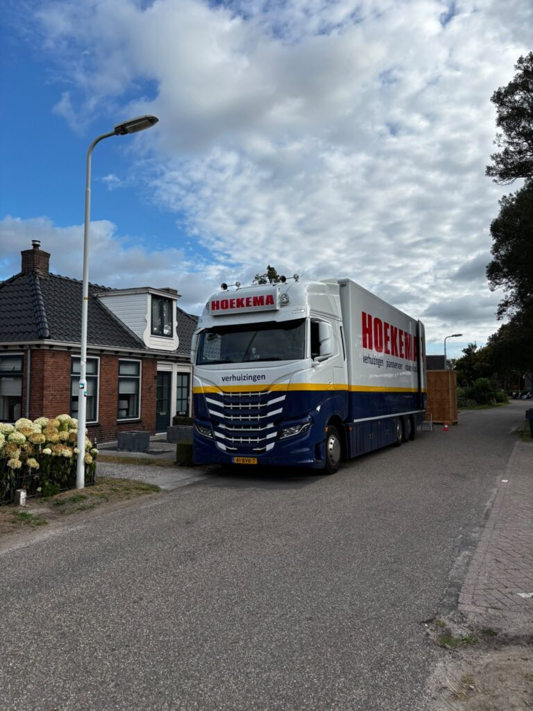 Verhuiswagen en opslagkist van Hoekema Verhuizingen bij een gebouw tijdens een projectverhuizing