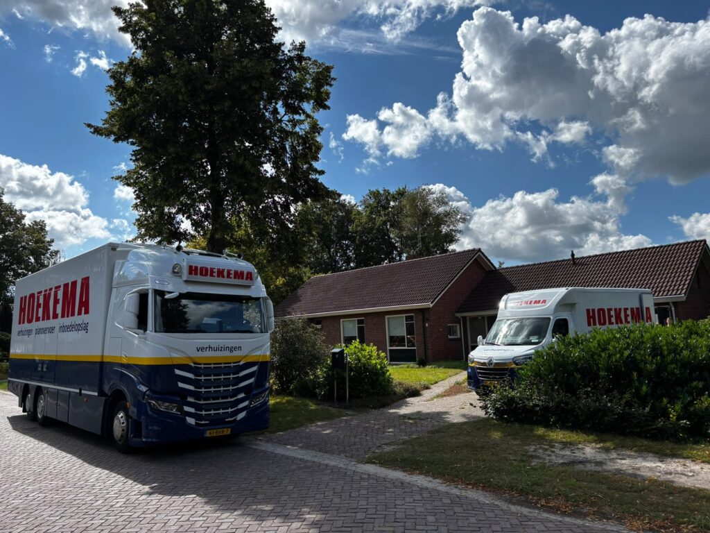 Twee verhuizers van Hoekema Verhuizingen dragen een piano bij de voordeur van een woning