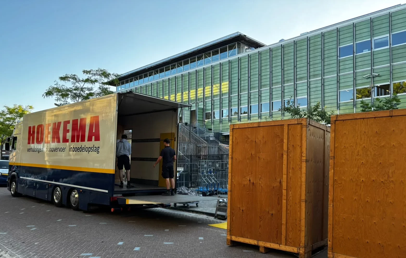 Verhuizers van Hoekema Verhuizingen laden naast houten opslagkisten tijdens een projectverhuizing