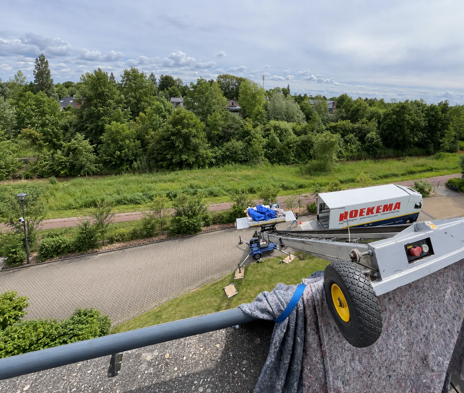 Verhuislift van Hoekema Verhuizingen reikt tot het balkon van een appartement, met de verhuiswagen op straat beneden